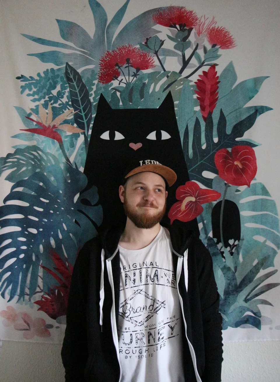 Thomas Ramsing foran et farverigt botanisk vægmaleri med en kat